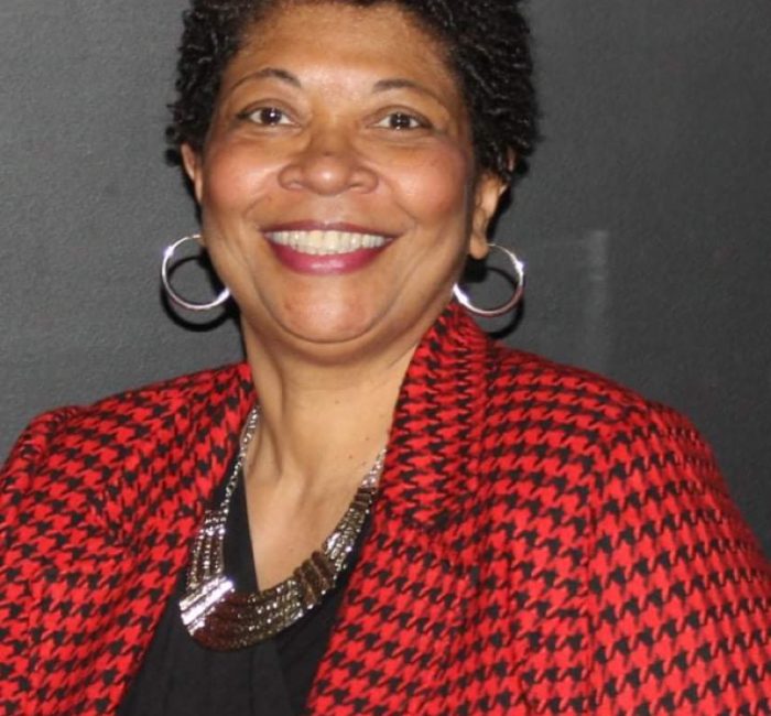 lady with short curly hair wearing red and black checkered jackey and gold hoop earringsa